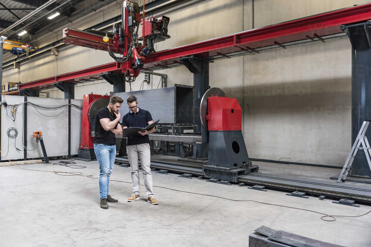Two men with folder standing on factory shop floor